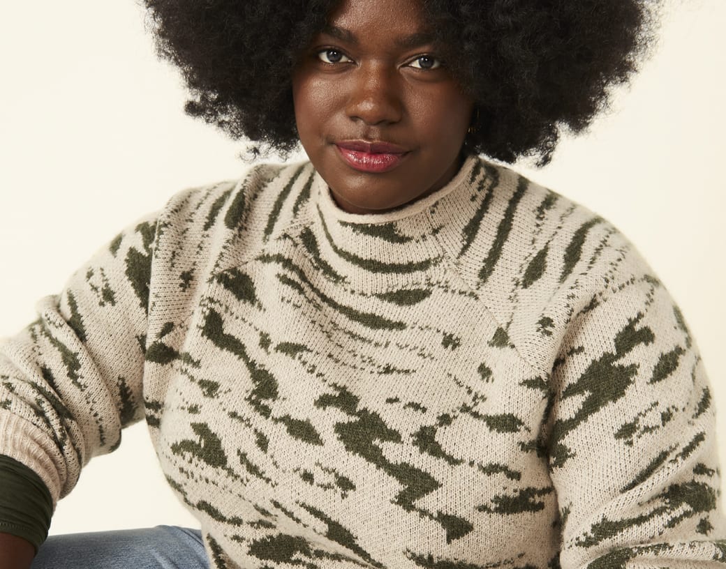 plus size woman in green and beige splattered print turtleneck and light wash jeans
